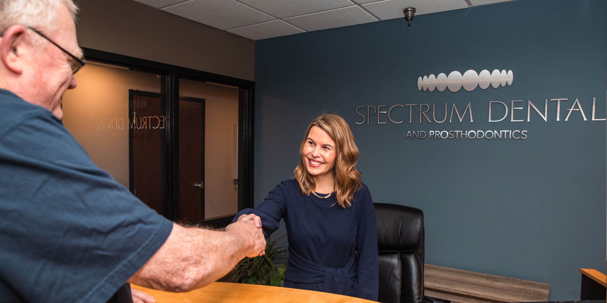 staff member shaking hands with patient at the front desk within the dental practice